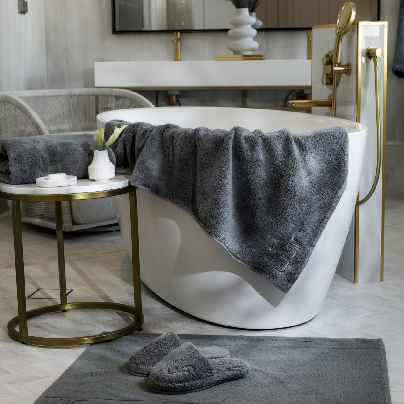 Modern bathroom with a white bathtub, gray towel, and slippers on a rug.