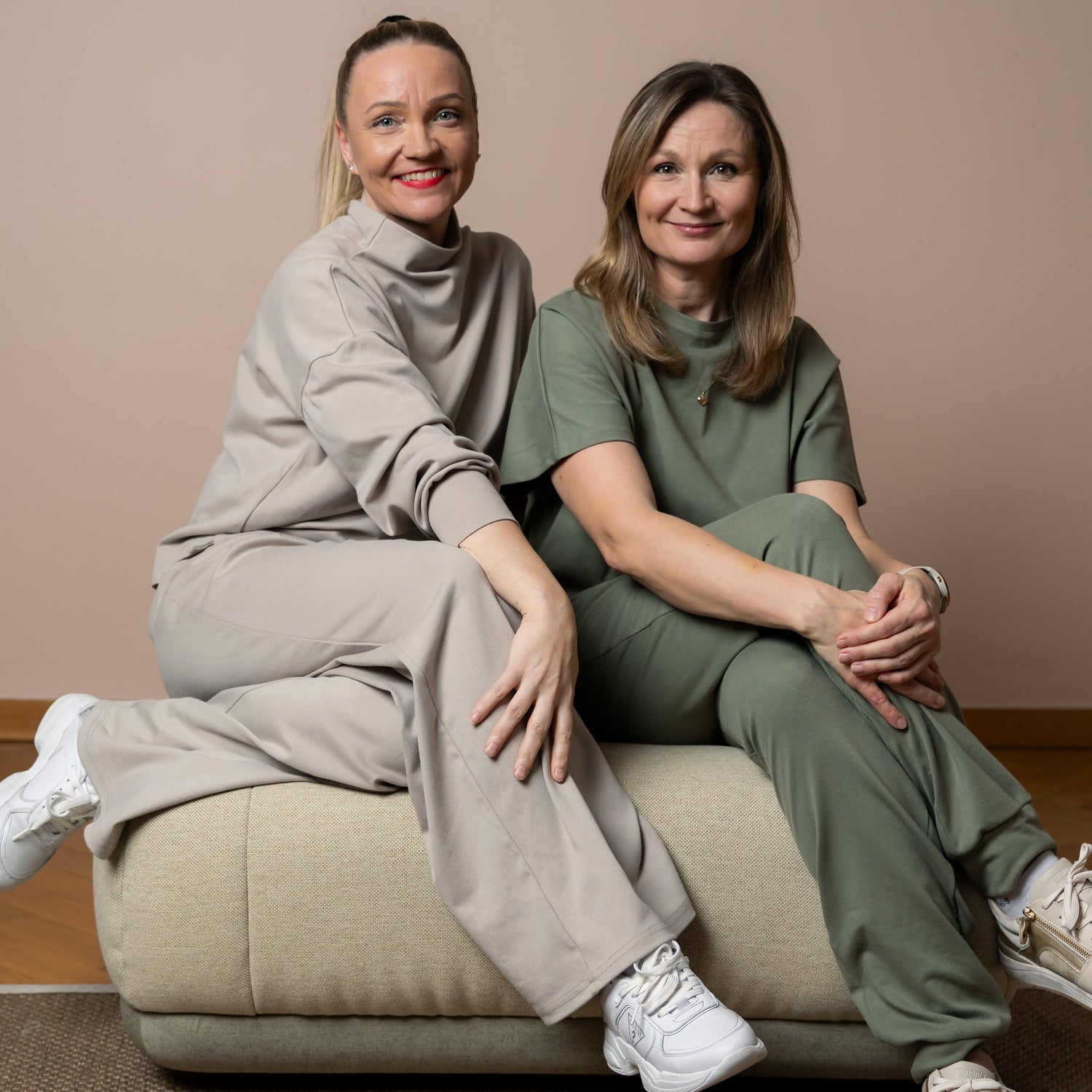 Two women sitting on a beige couch against a plain wall.