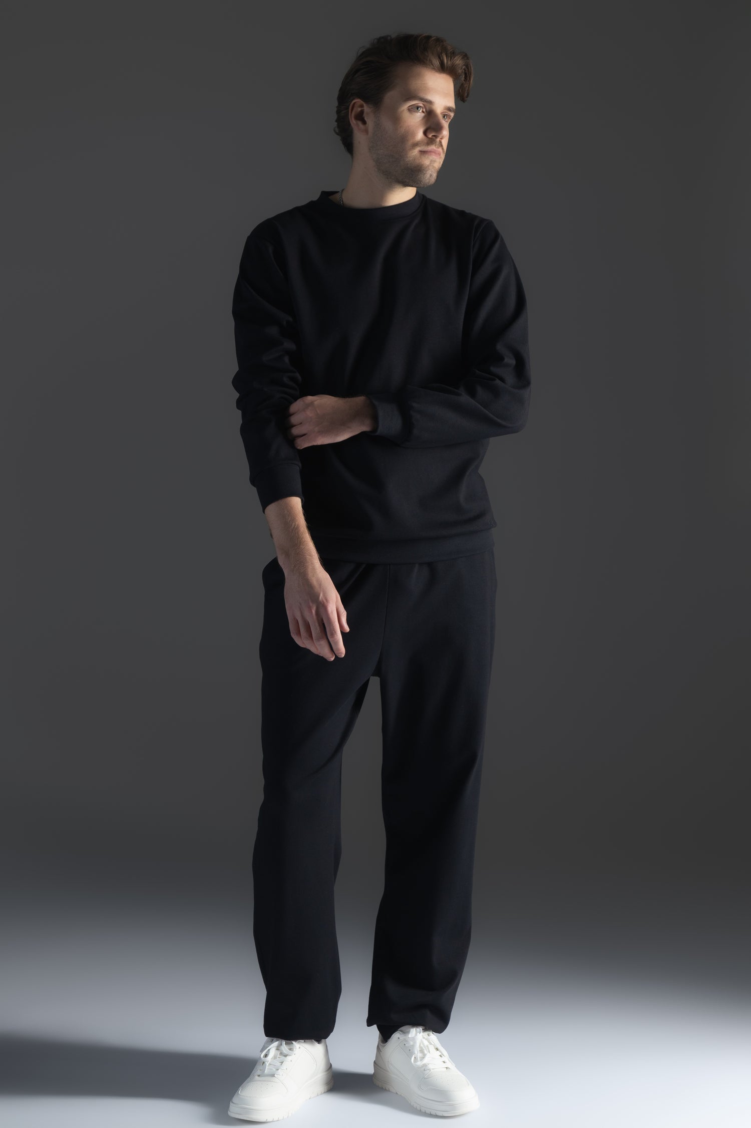 Man wearing a black outfit with white shoes on a gray background