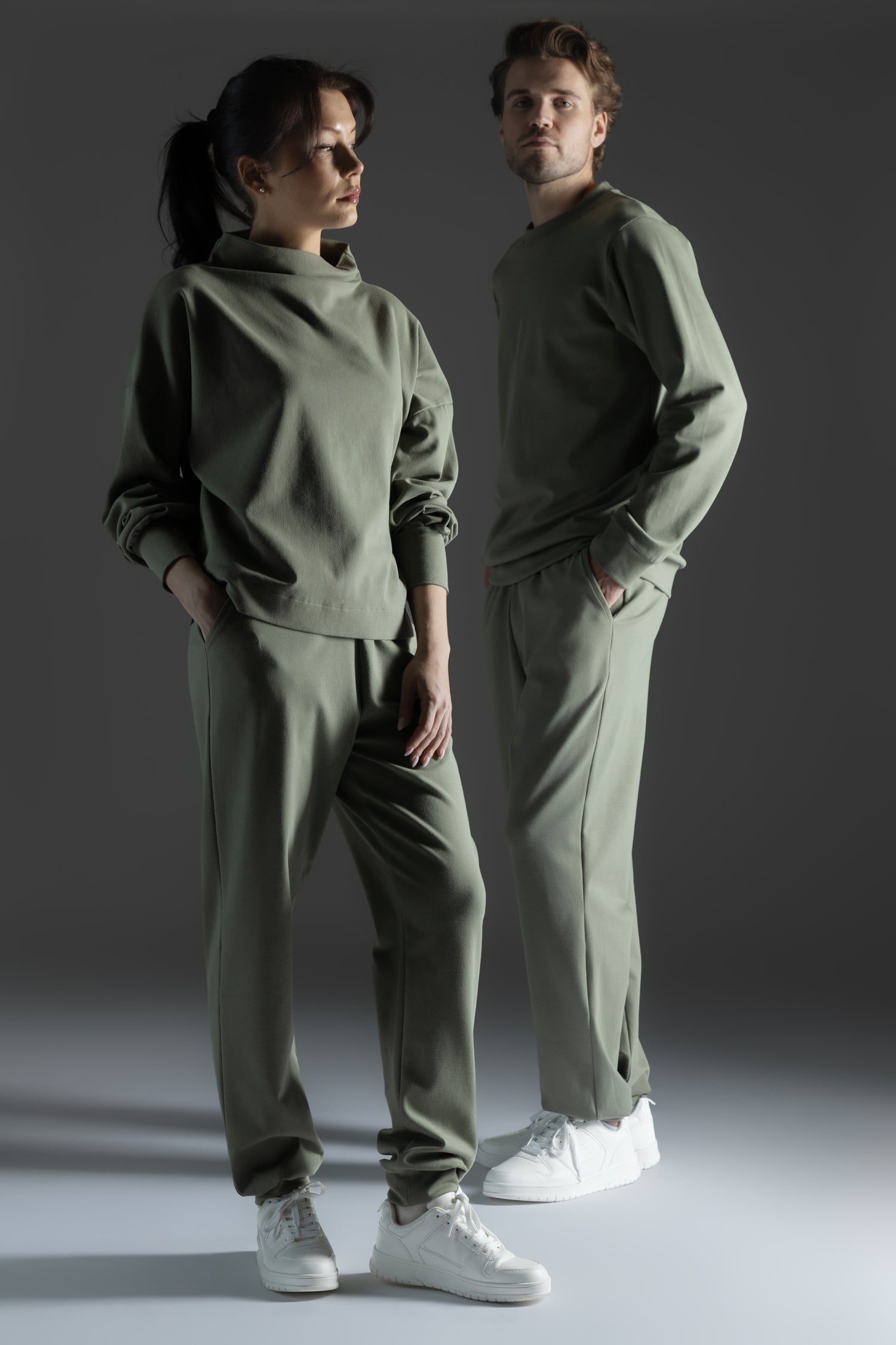 Two people wearing matching green outfits standing against a dark background