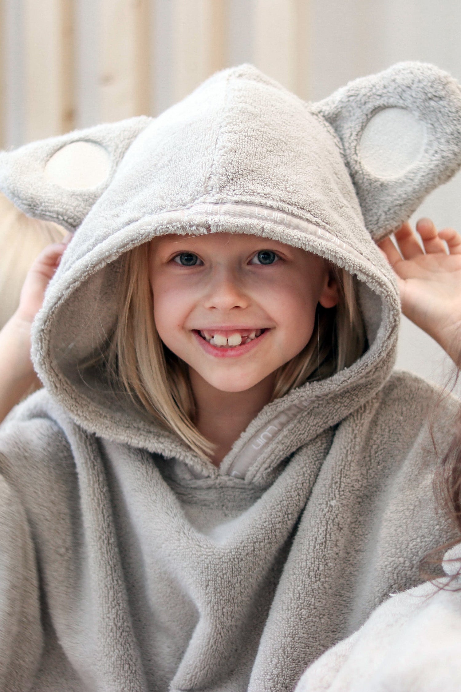 Child wearing a beige hooded poncho with bear ears, sitting on a couch.