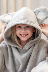 Child wearing a beige hooded poncho with bear ears, sitting on a couch.