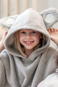 Child wearing a beige hooded poncho with bear ears, sitting on a couch.