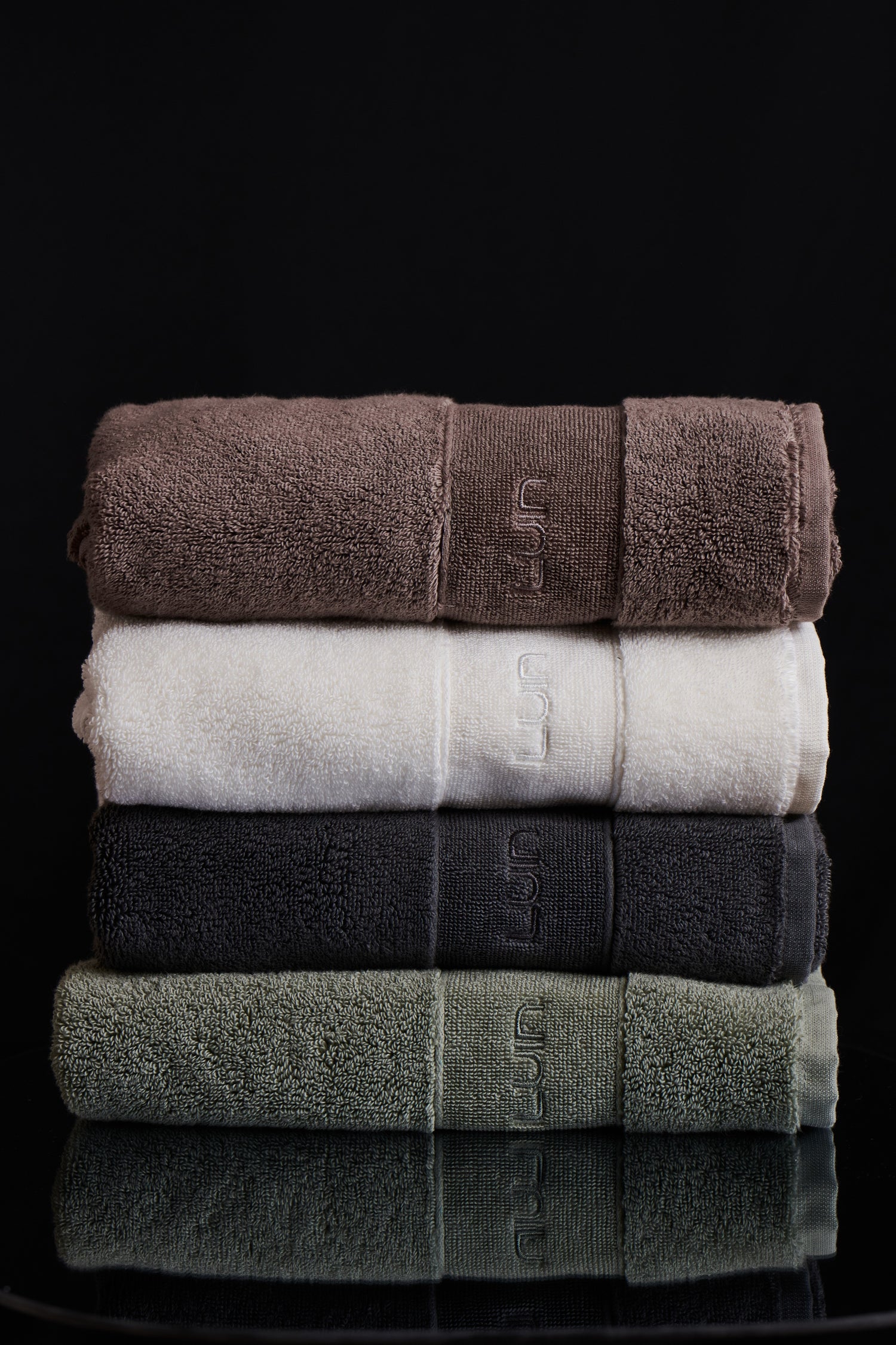 Stack of folded towels in brown, white, black, and green on a black background